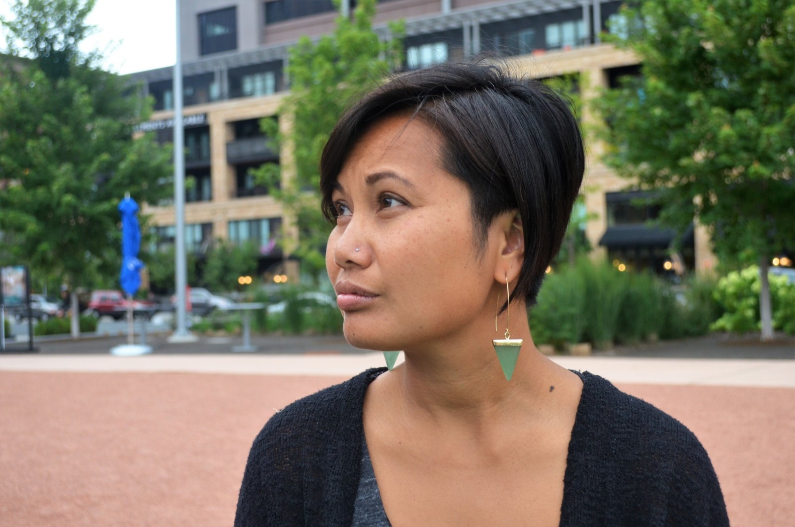 Portrait of Kaysone Syonesa in profile wearing green triangle earrings, outdoors in a plaza