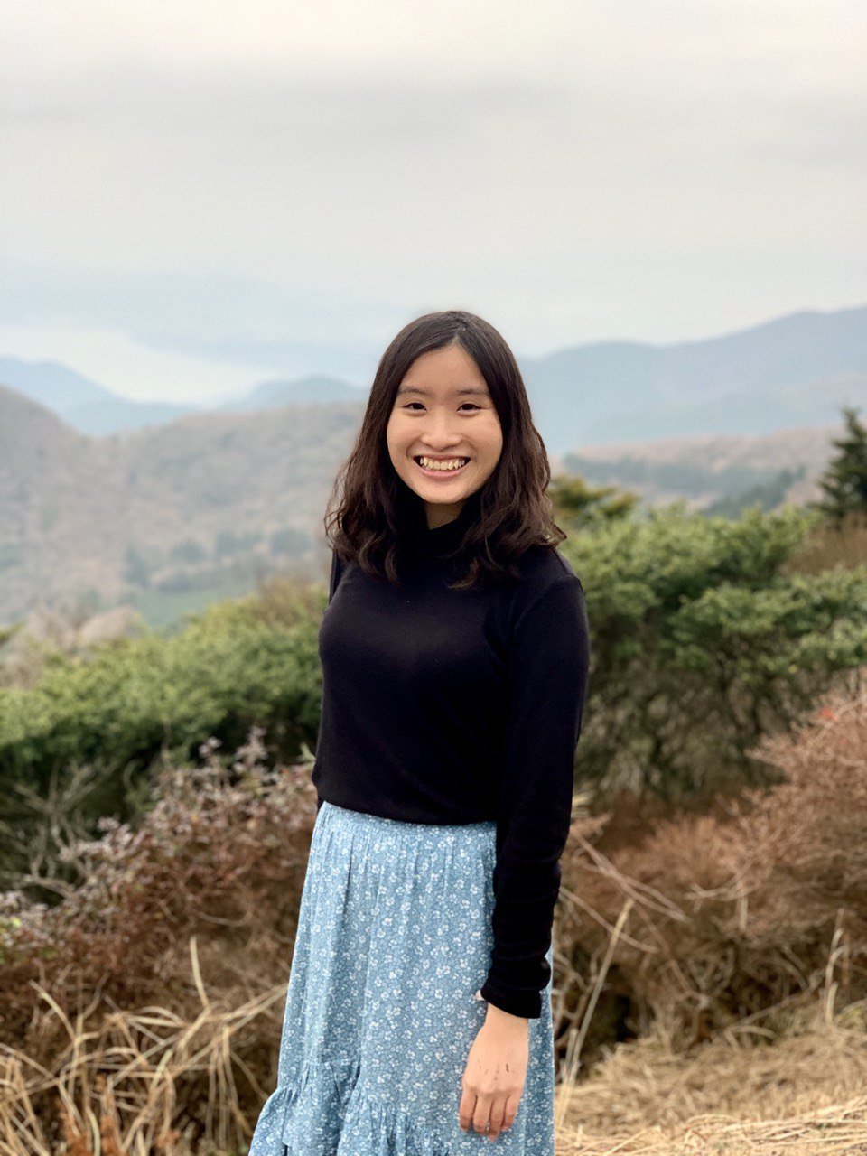 Sarah Ang smiling outdoors with misty mountains behind her
