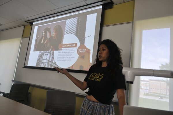 Woman in a black 'Lao in the House' T-shirt presenting in front of a slide titled 'I am an artist.'