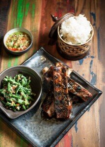 Grilled spareribs with stir-fried long beans, a chili dip, and sticky rice in a woven basket