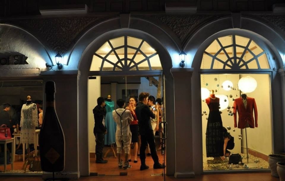 Evening crowd inside an arched boutique window with gowns and a red jacket on display