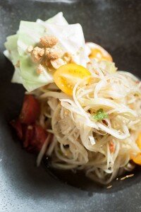 Close-up of green papaya salad topped with cherry tomatoes, peanuts, and a cabbage leaf