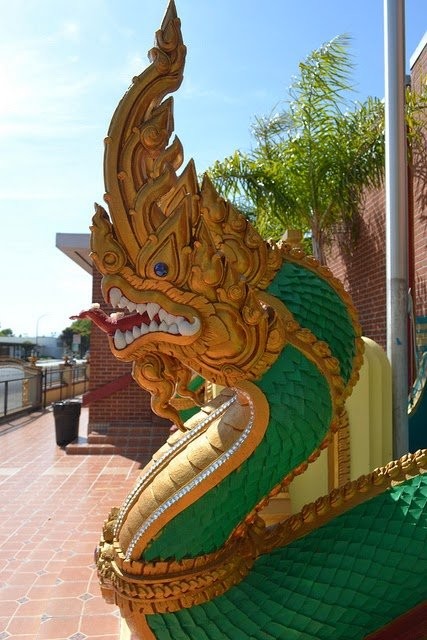 Golden and green Nak serpent statue with open jaws guarding a temple entrance under a blue sky