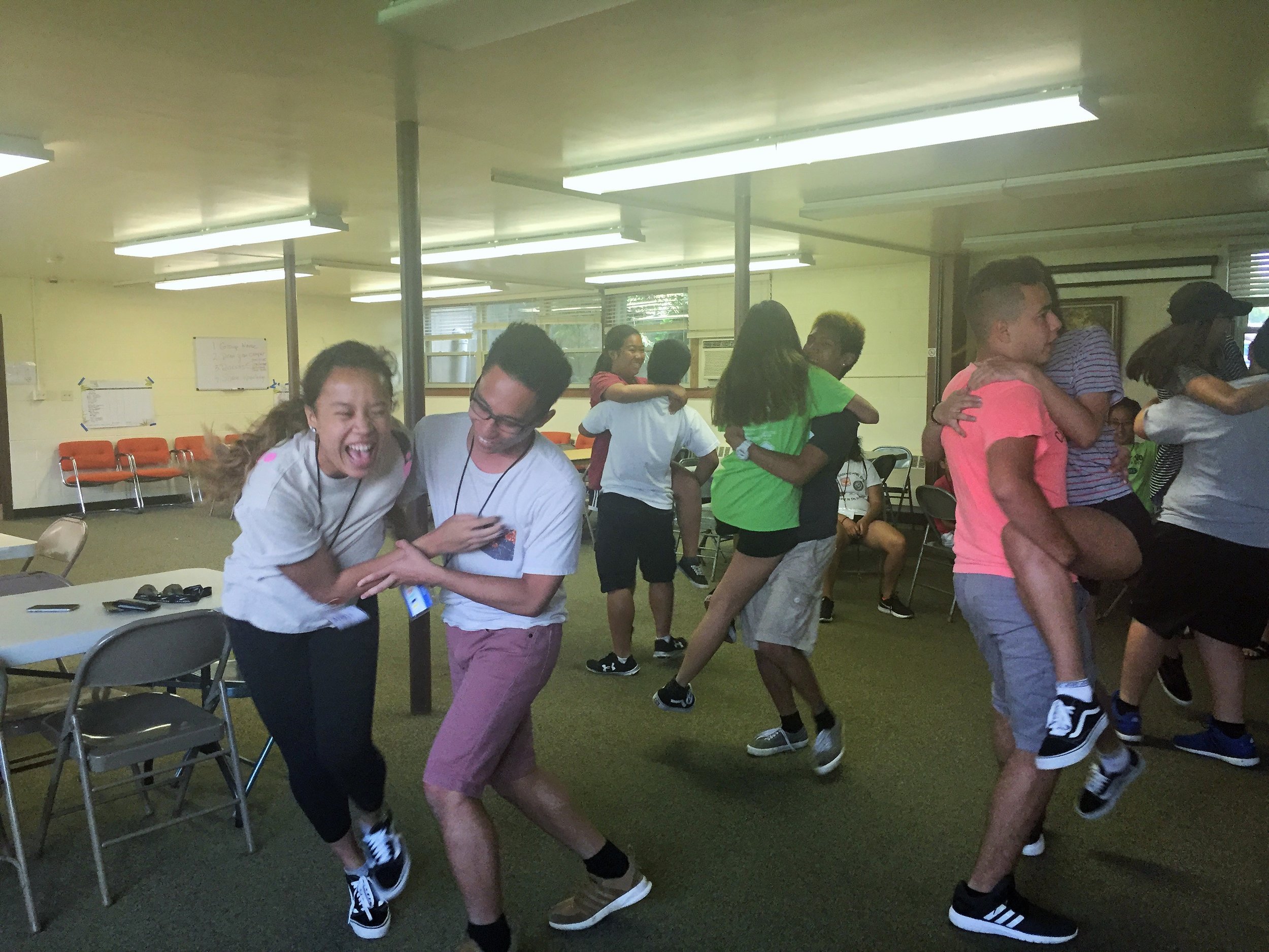 Teens laughing and giving each other piggyback rides in a community hall.