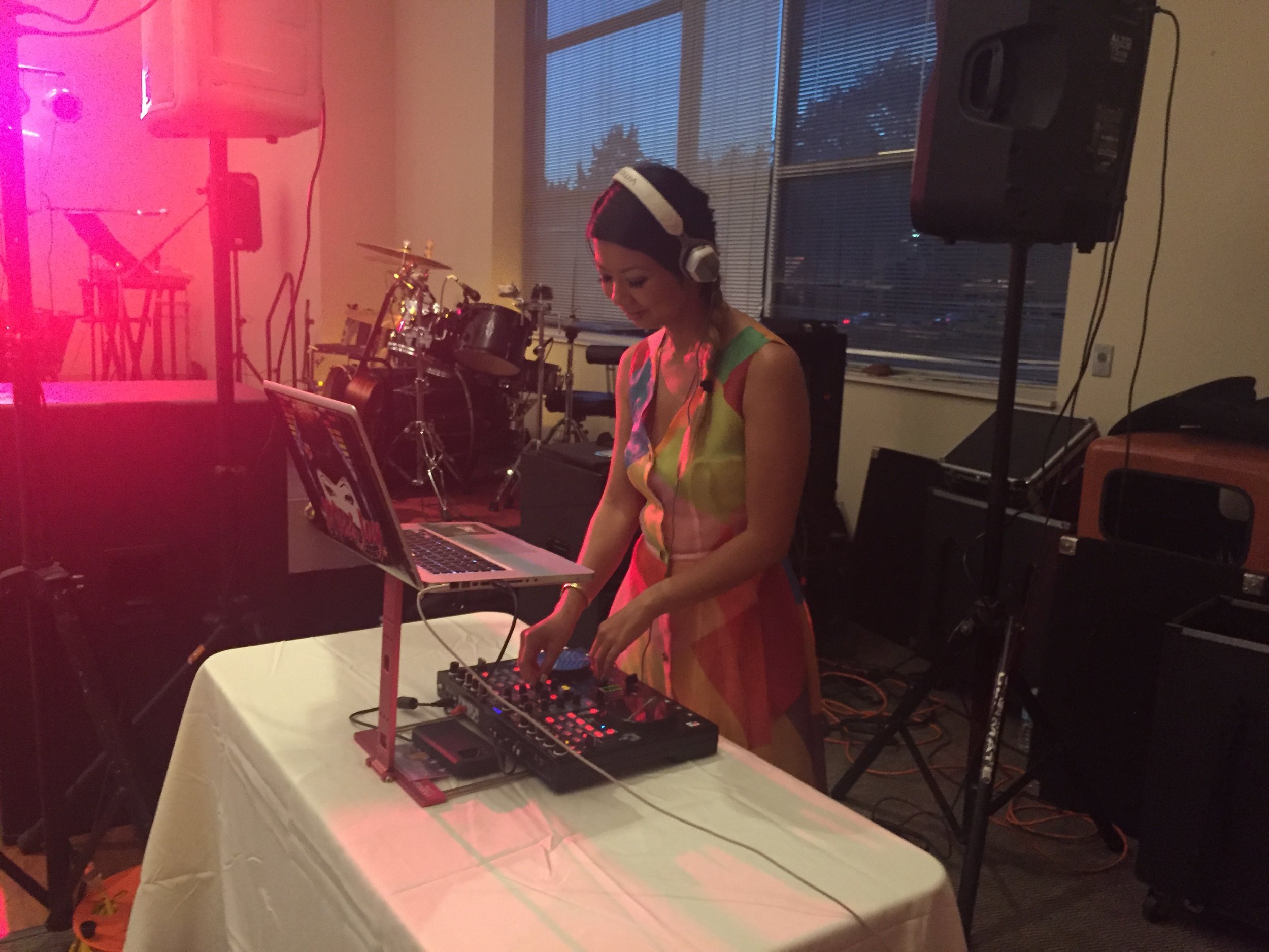 Woman in headphones and a colorful dress DJing at a mixer and laptop on a table at an event.