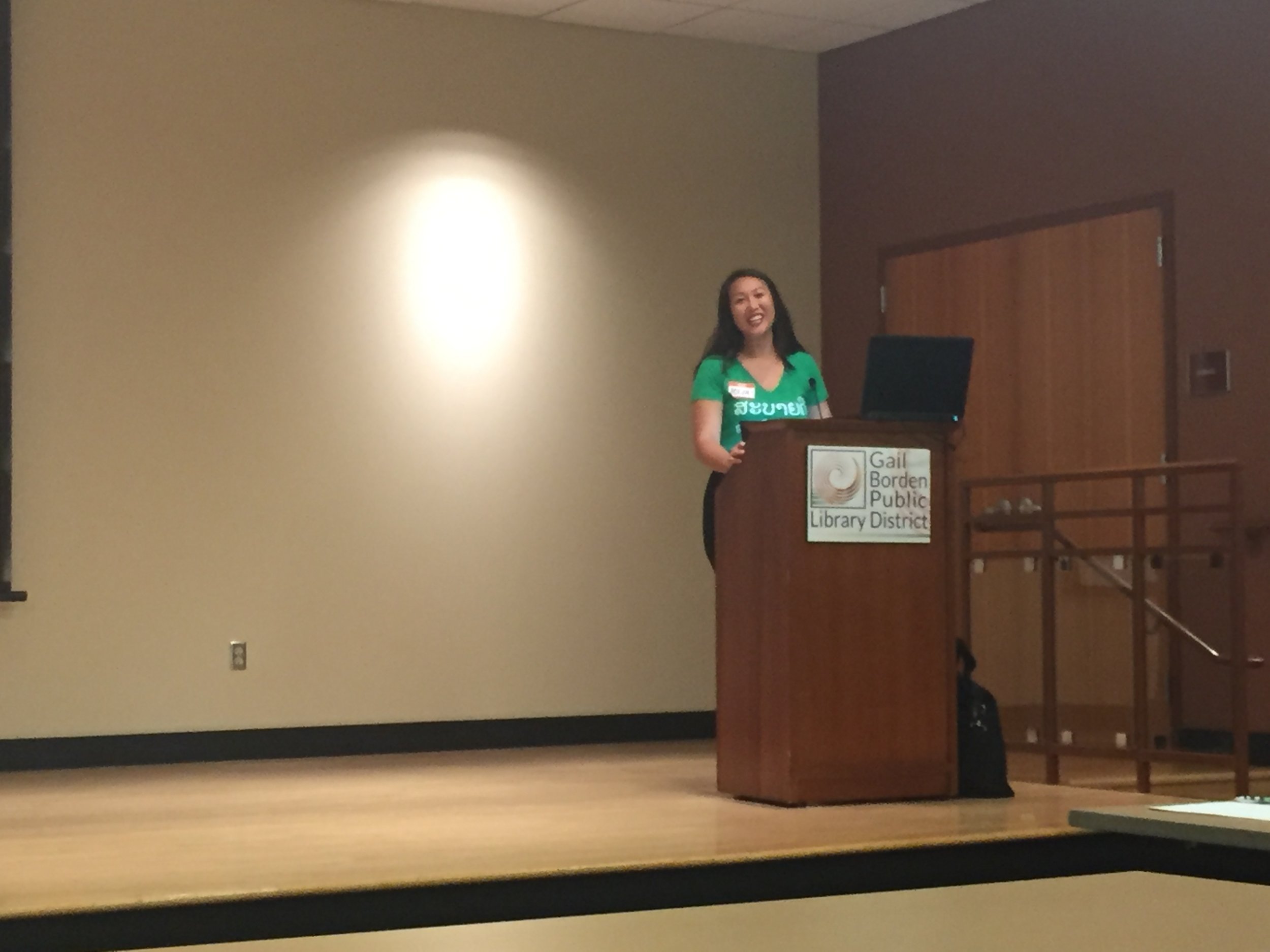 Smiling woman in a green shirt speaking at a Gail Borden Public Library District podium.
