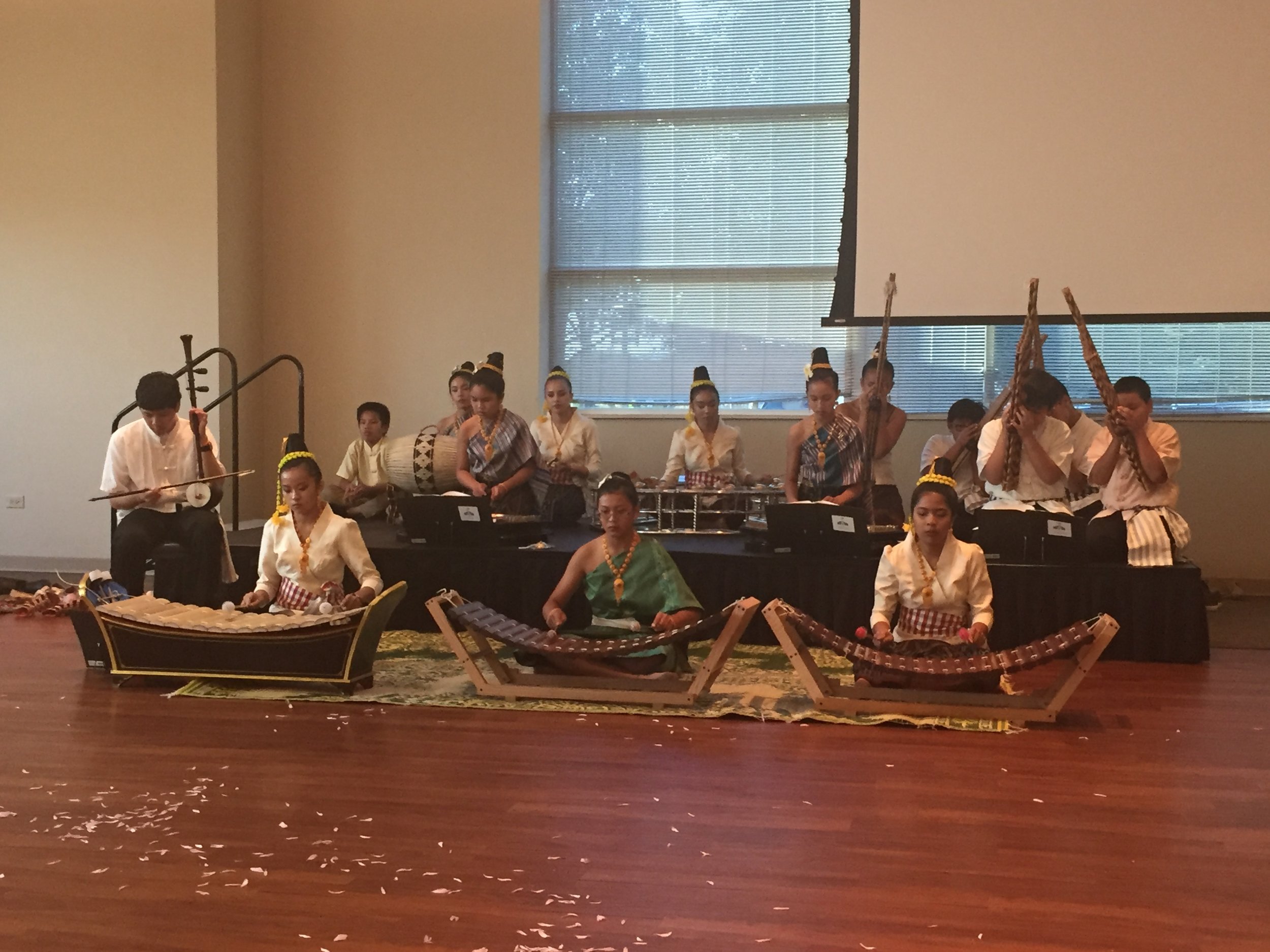 Lao youth in traditional dress playing a Lao music ensemble, with ranat xylophones in front and khaen and drums behind.