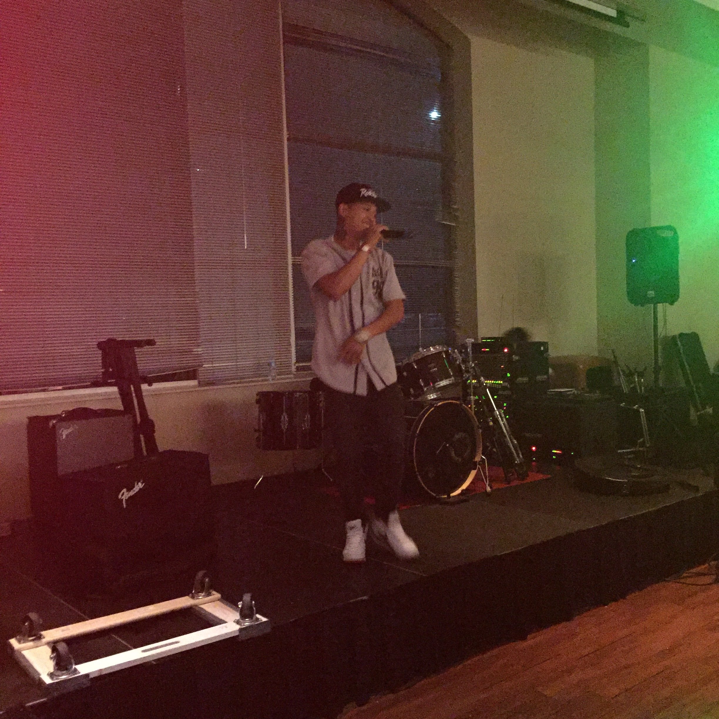 Young man in a cap and baseball jersey rapping into a microphone on a small stage.