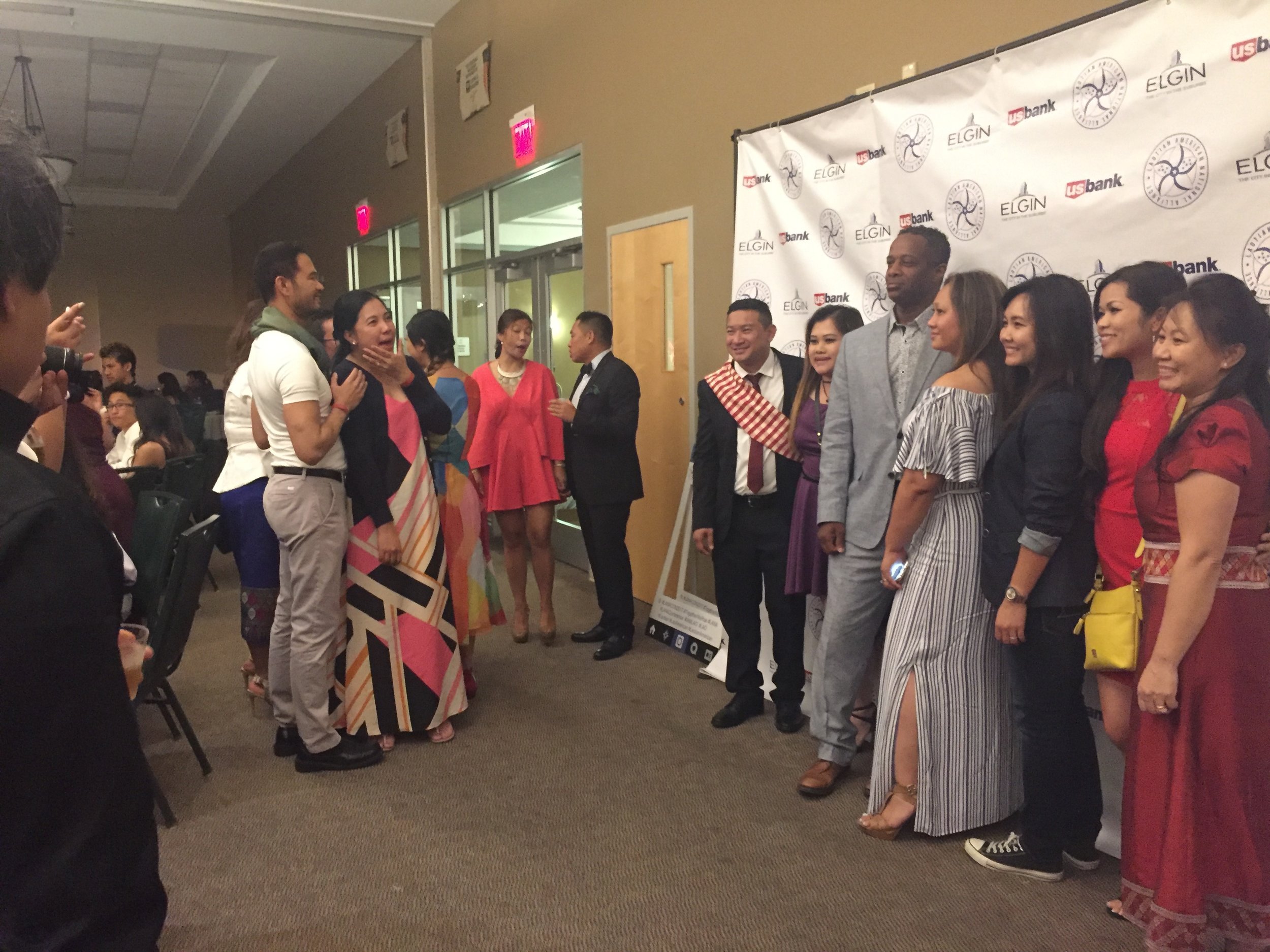 Guests in formal wear and Lao sinh posing for photos in front of an Elgin sponsor backdrop.