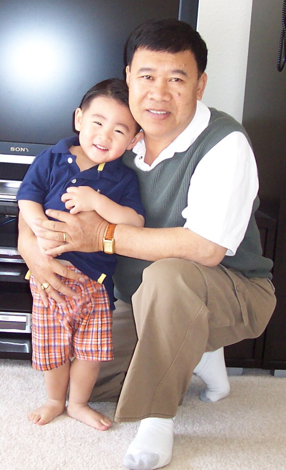 Older man kneeling and hugging a smiling toddler in a living room