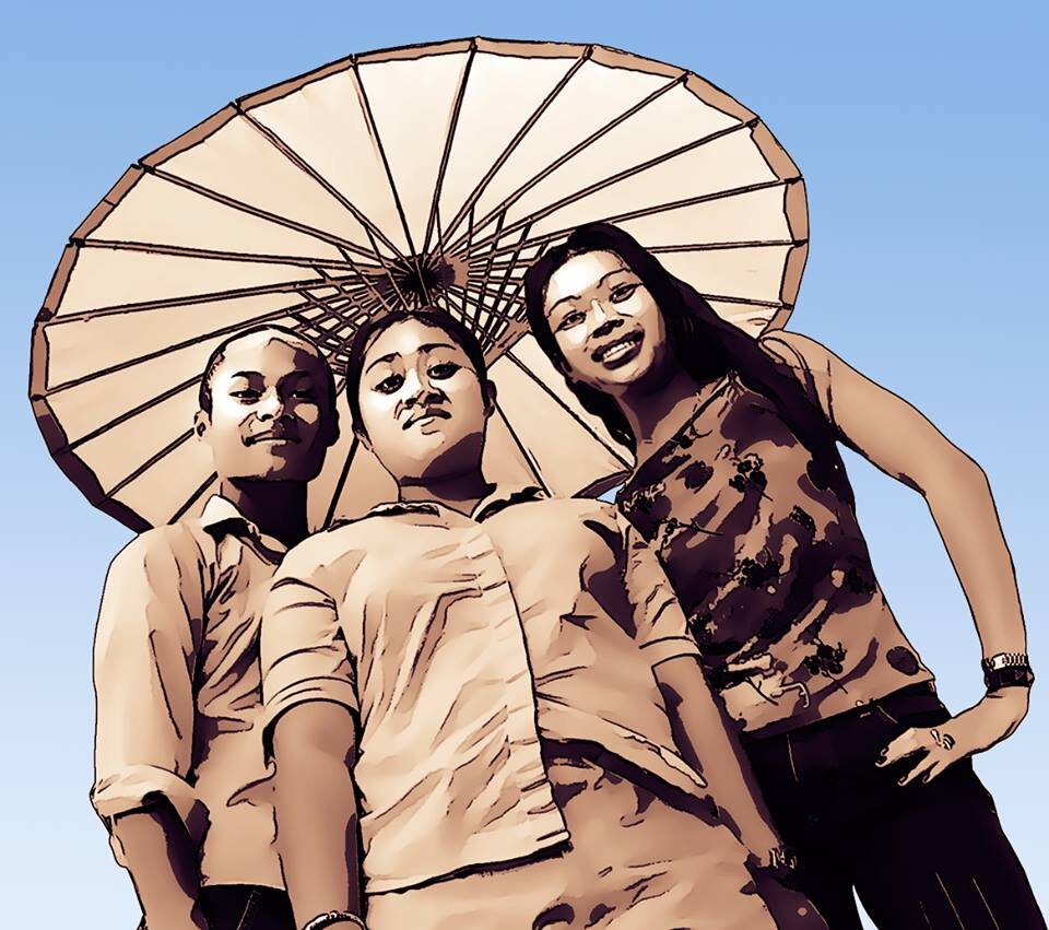 Stylized photo of three young people posing under a large paper parasol against a blue sky