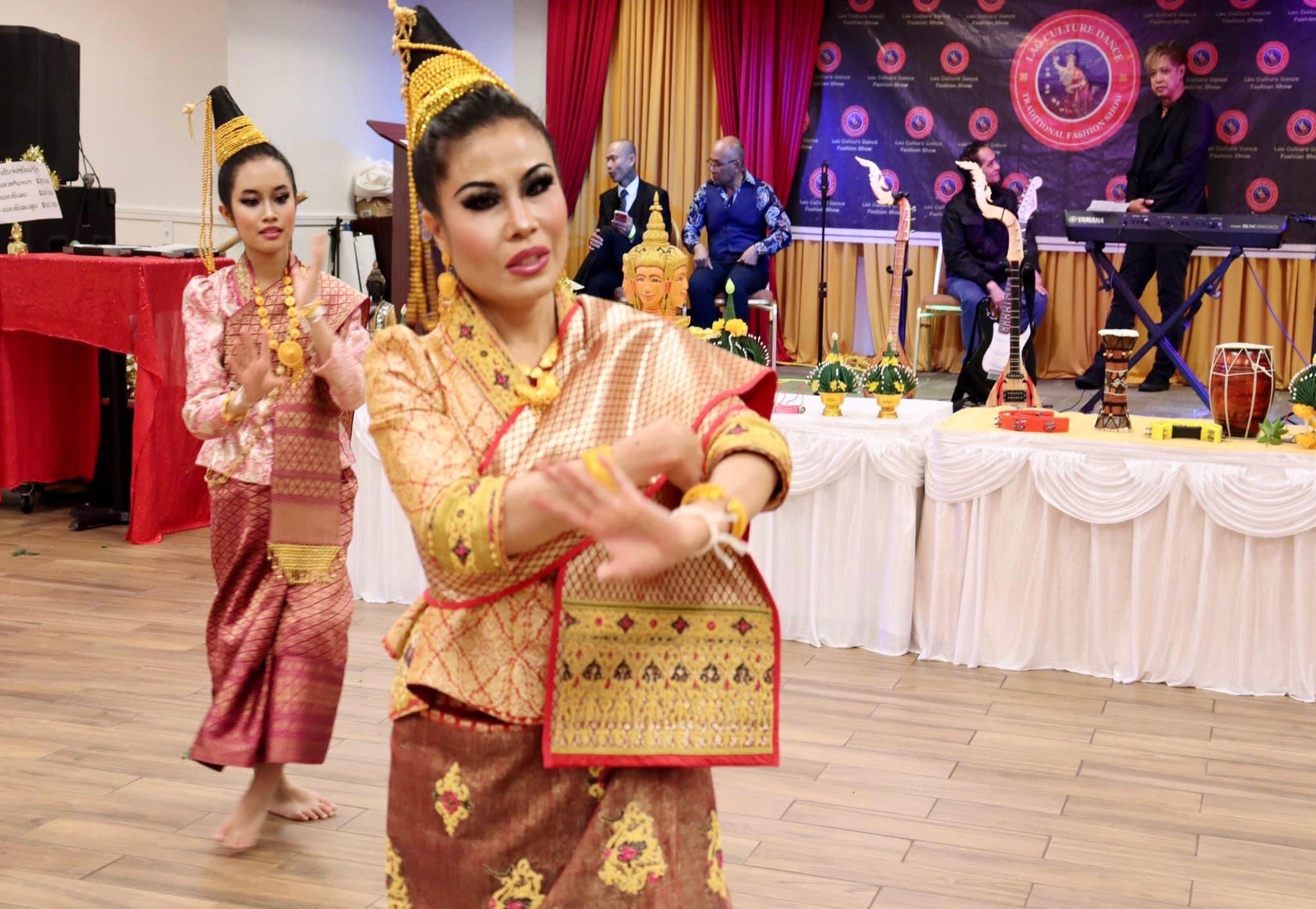 Two Lao classical dancers in pointed gold headdresses perform hand gestures before a live band