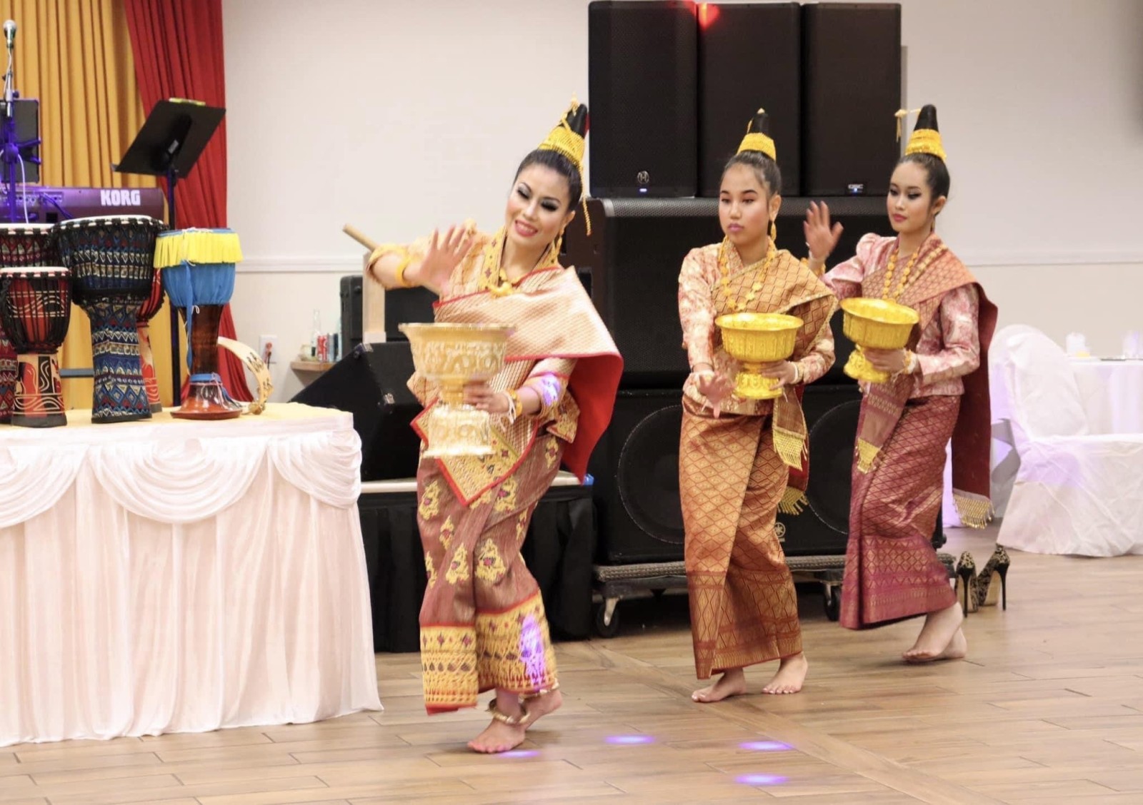 Three dancers in traditional Lao costumes carry gold offering bowls in the Wishing dance