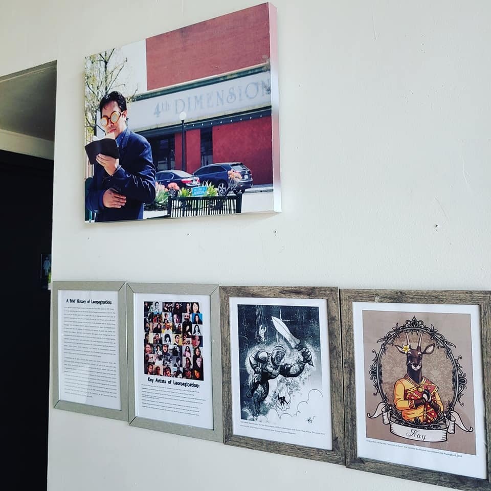 Laomagination retrospective exhibit on a wall: a large photo of a poet reading outside 4th Dimension, and framed history panels and artworks