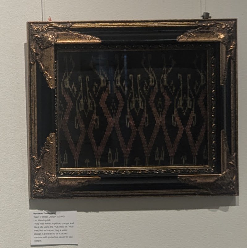 Framed Lao silk weaving with rows of Nak motifs in gold and rust on black, in an ornate gold frame