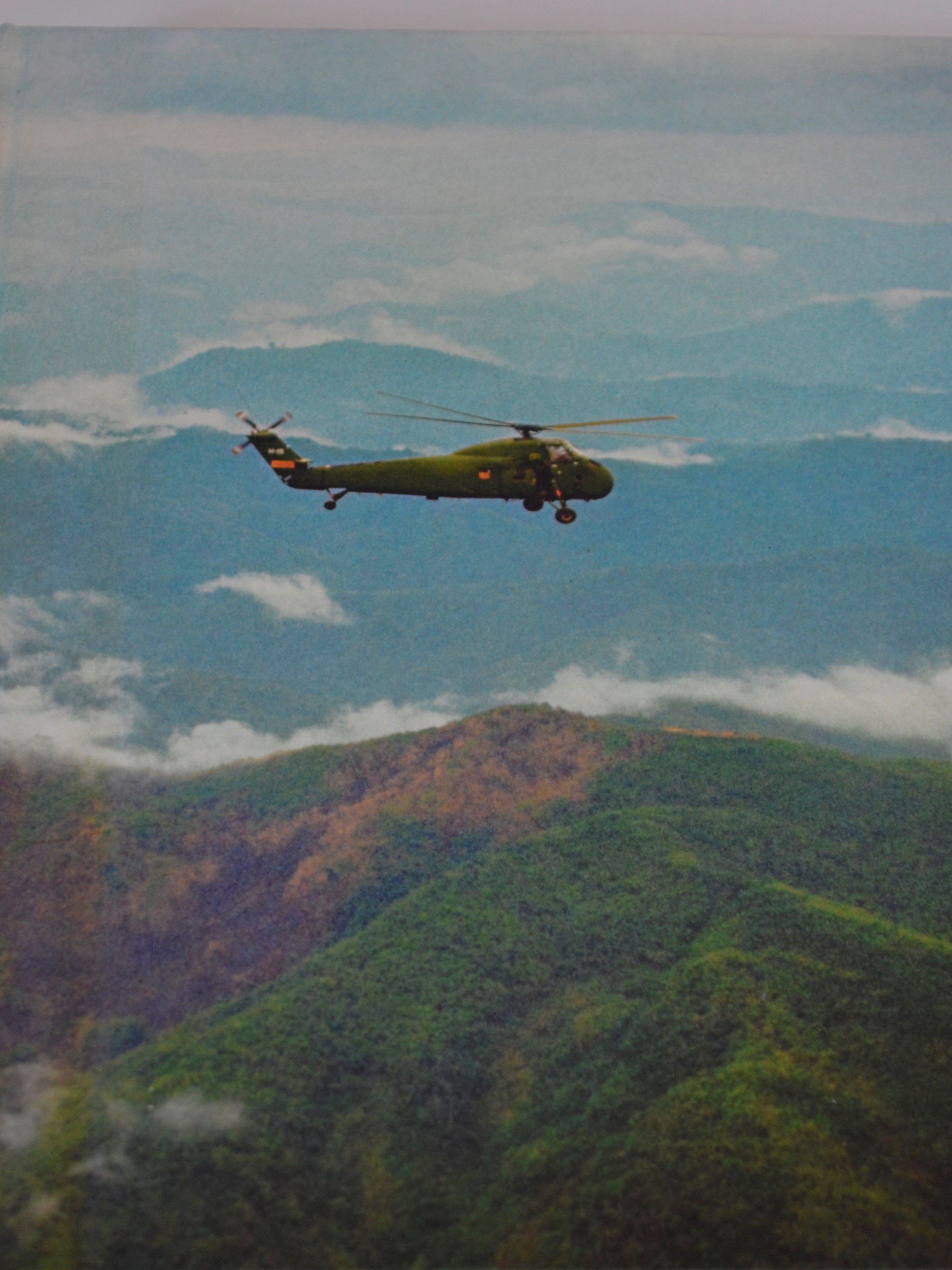 Vintage photo of a military helicopter flying over forested mountains in Laos