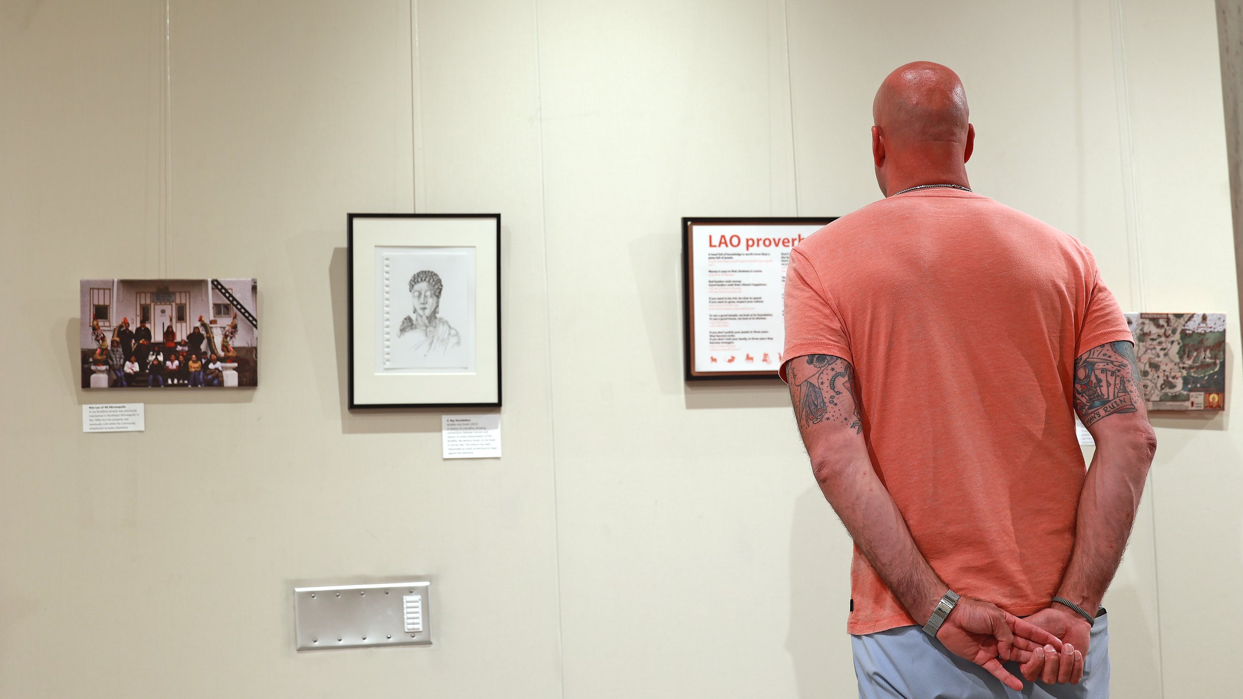 Visitor viewing Laomerica 50 exhibit works, including a portrait drawing and a Lao proverbs panel