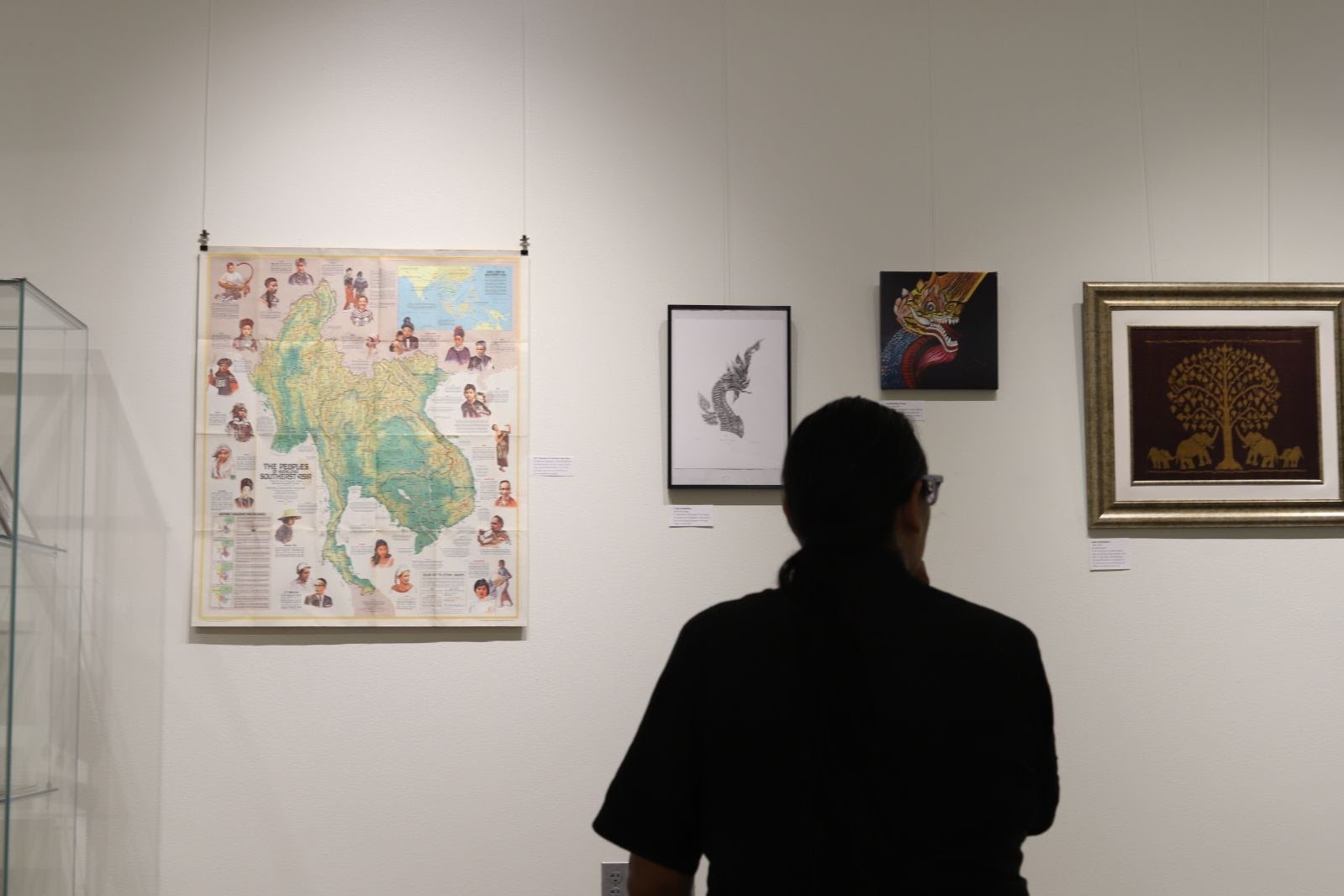 Visitor viewing a map of Laos and framed artworks, including a Nak and a golden tree, at Laomerica 50
