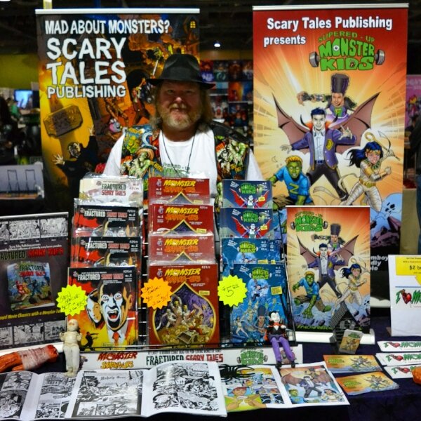 Man in a black hat behind the Scary Tales Publishing table stacked with Monster Kids and Fractured Scary Tales comics