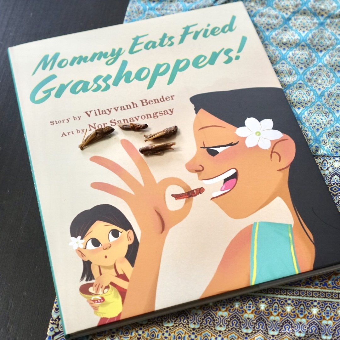 Cover of Mommy Eats Fried Grasshoppers! by Vilayvanh Bender, art by Nor Sanavongsay, with real fried grasshoppers resting on the book