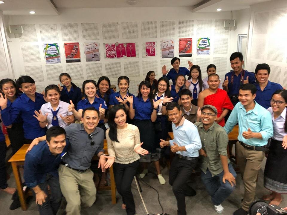 Large group of students in blue uniforms, a monk, and filmmakers posing with thumbs up after a screening