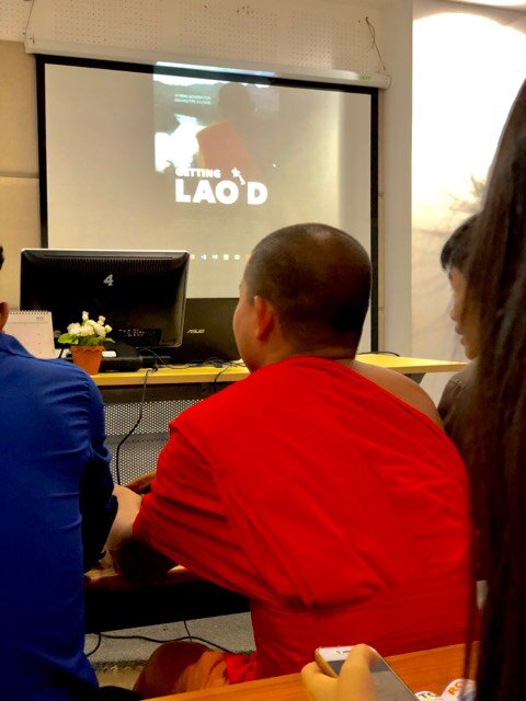 Monk in saffron robes watching a projected screening of Getting Lao'd