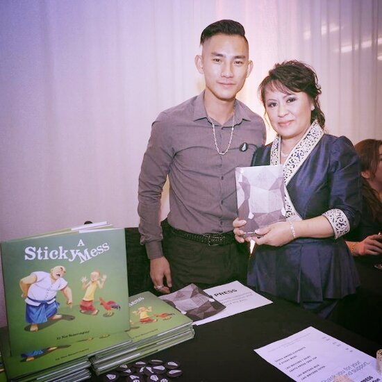 Krysada Panusith Phounsiri and a woman holding a book beside a table stacked with copies of A Sticky Mess