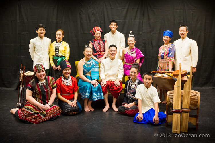 Performers in traditional dress from several ethnic groups of Laos posing on stage with a khaen and a drum
