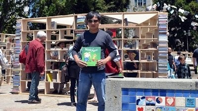 Man holding A Sticky Mess at the Bay Area Book Festival, standing in front of wooden bookshelves