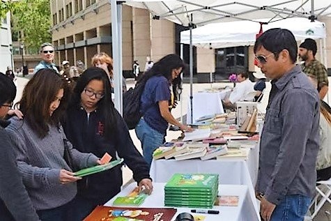 Visitors browse children's books at the Sahtu Press table under a tent at the Oakland Book Festival