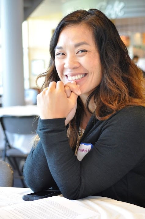 Sisavanh Phouthavong smiling at a table, chin resting on her hands, wearing a name tag
