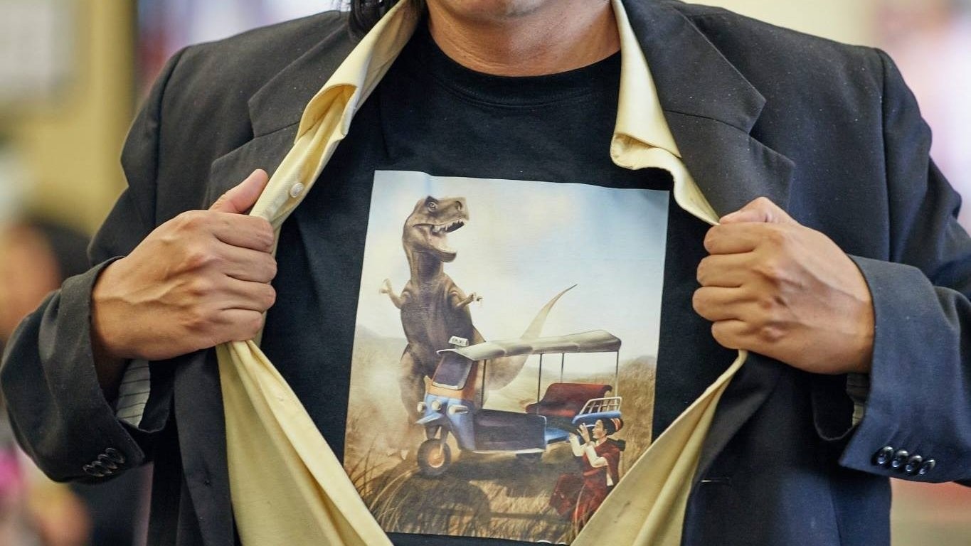 Man opening his jacket to reveal a T-shirt of a T. rex chasing a tuk-tuk.