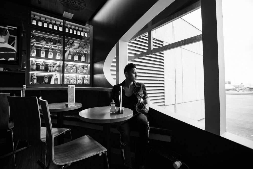 Black and white photo of a man seated by a large window in a dim bar