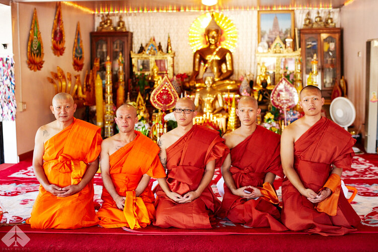 Five Buddhist monks in saffron robes kneeling before a golden Buddha altar