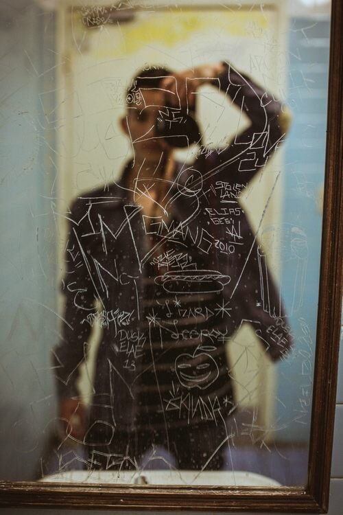 Photographer's reflection in a mirror covered with scratched graffiti