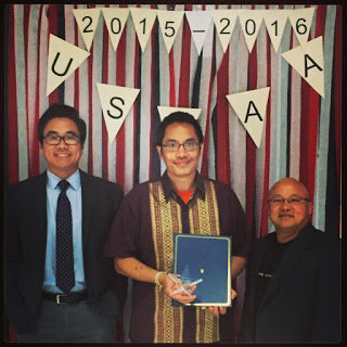 Three men stand under a USEAA 2015-2016 banner, the man in the center holding an award plaque