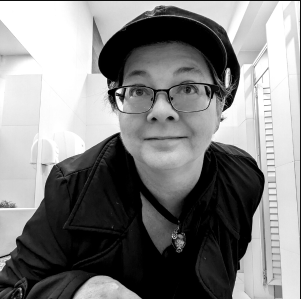 Black and white photo of Angela Yuriko Smith in glasses and a cap, smiling slightly