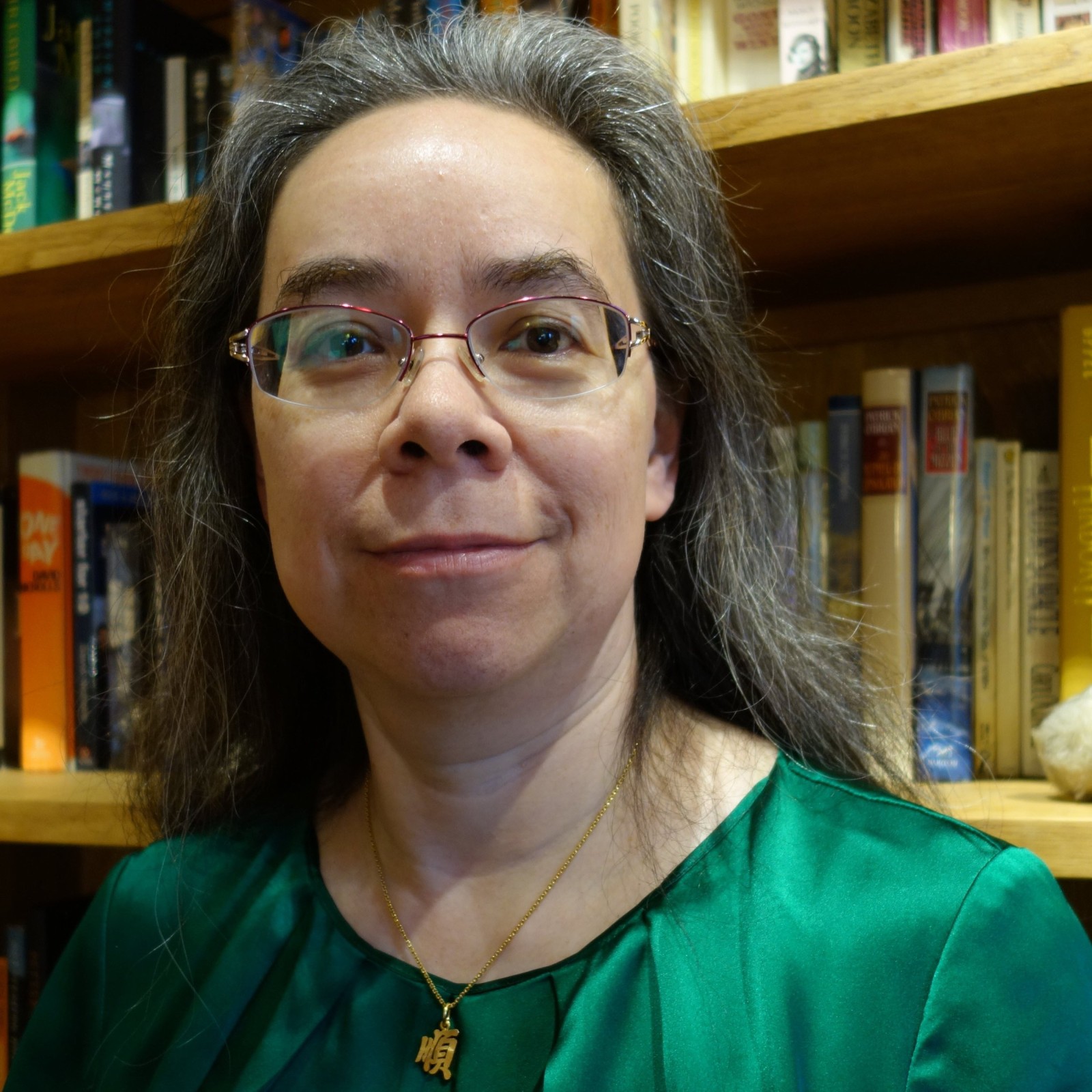 Portrait of poet Mary Soon Lee in a green blouse in front of bookshelves