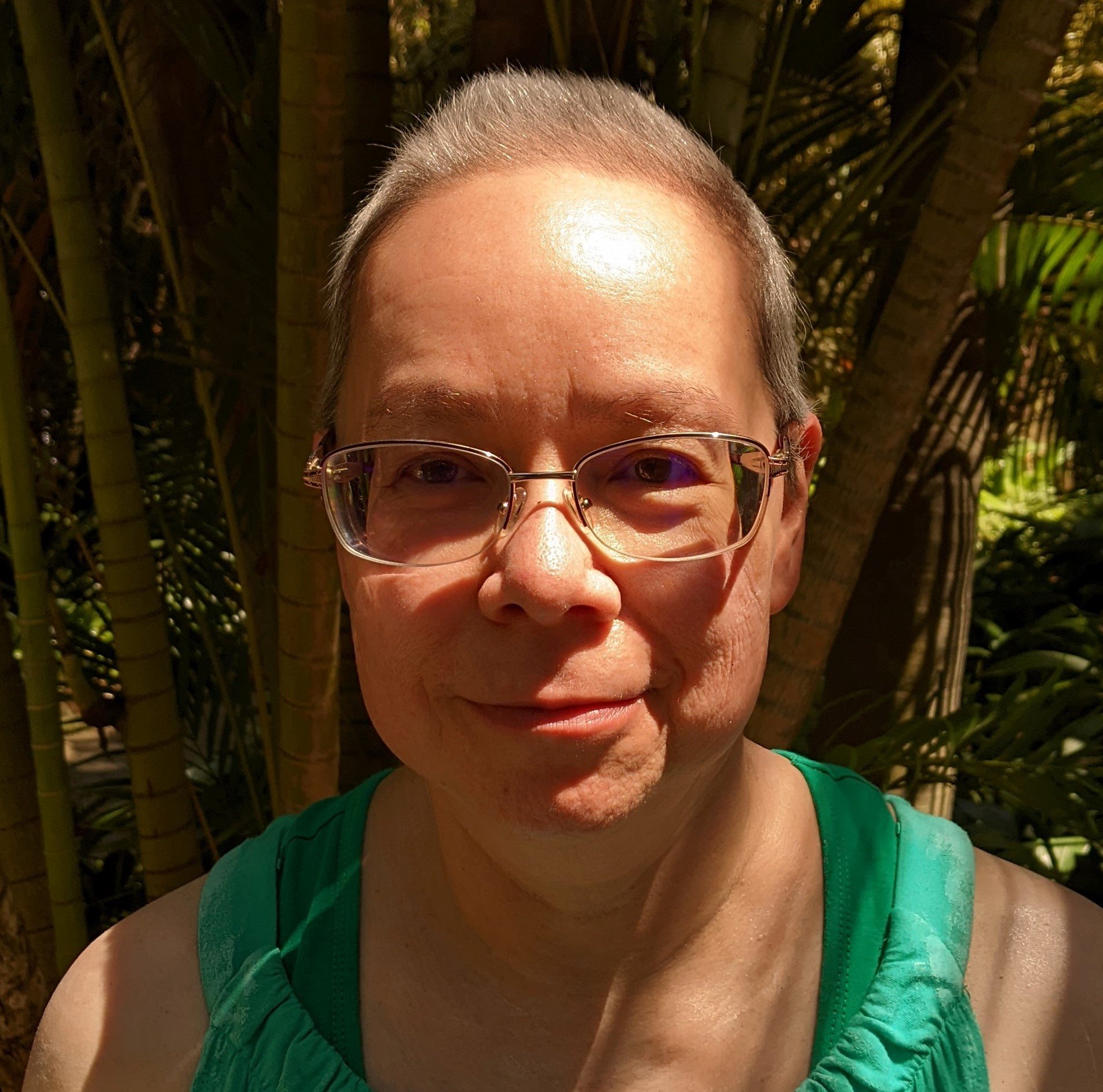 Portrait of Mary Soon Lee smiling in glasses among palm trees