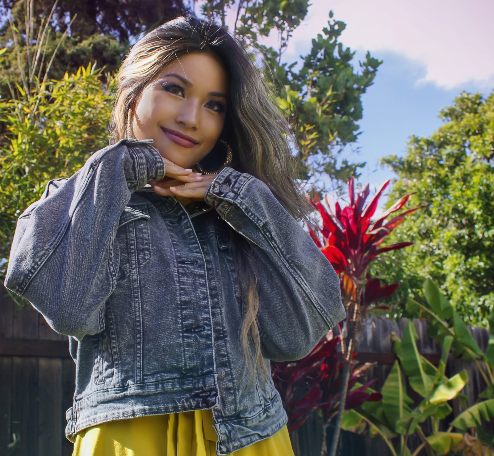 Amy Linsamouth posing outdoors in a denim jacket among tropical plants