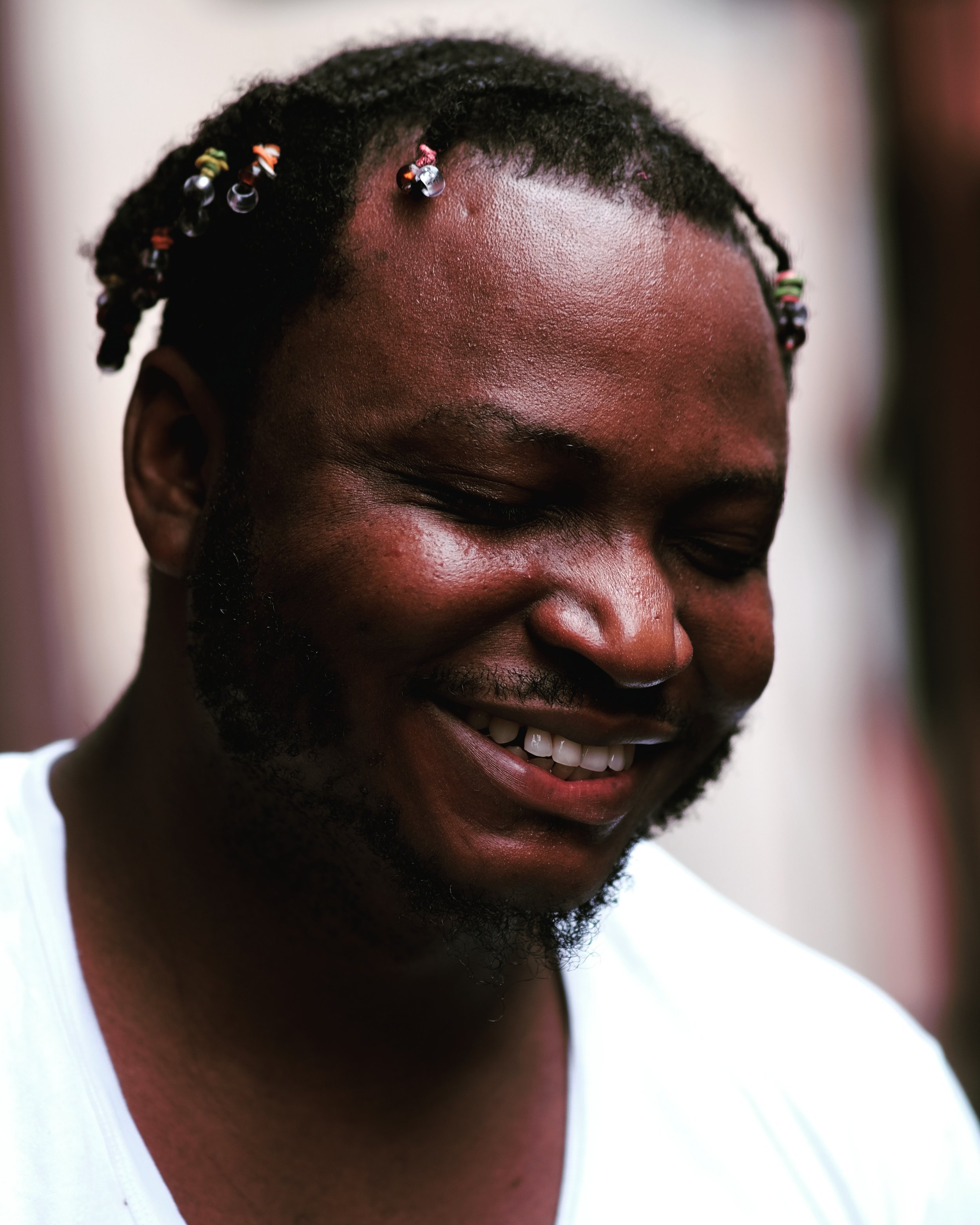 Hannu Afere smiling and looking down, with colorful beads in his hair