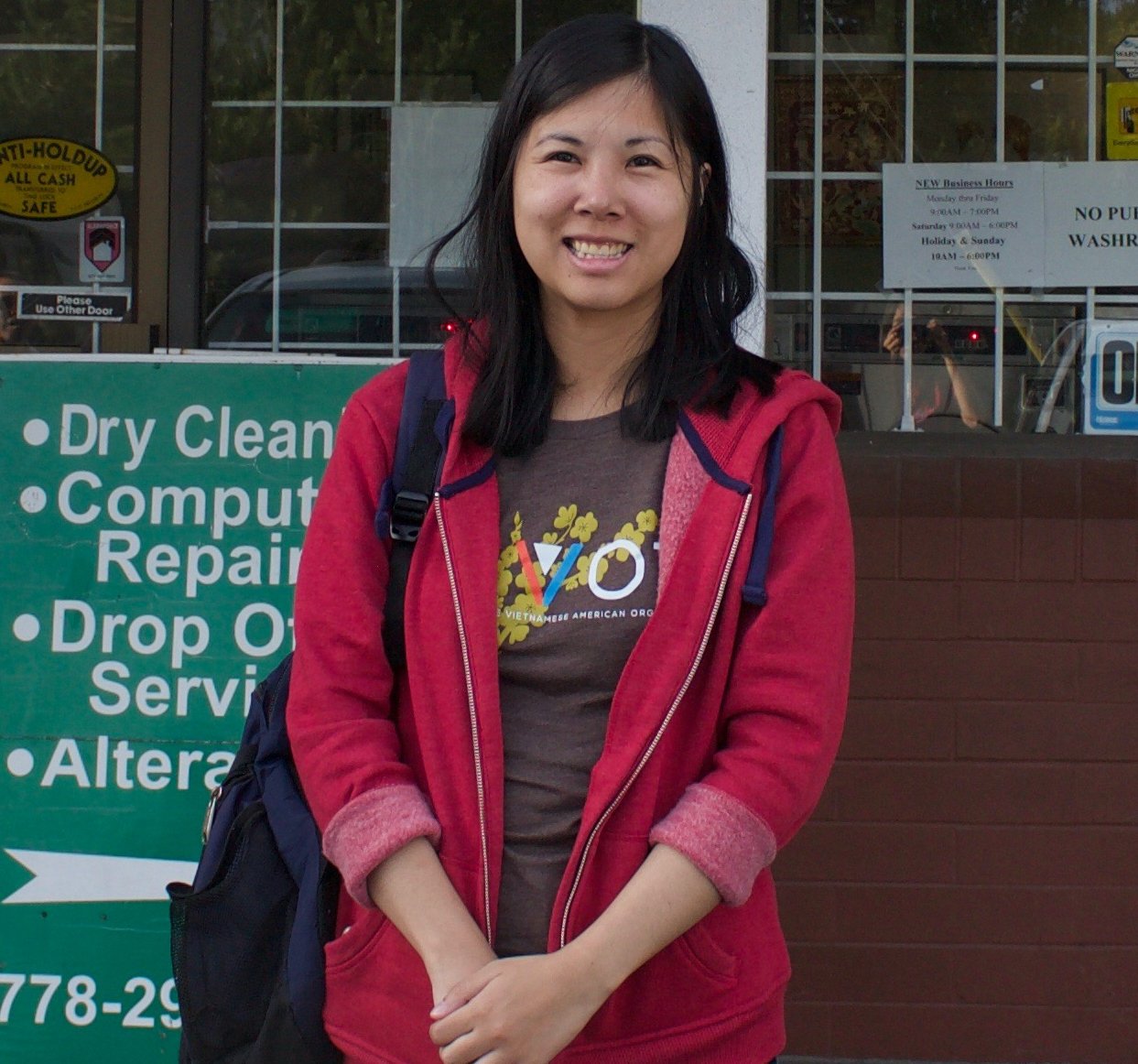 Jenna Le smiling in a red hoodie in front of a storefront