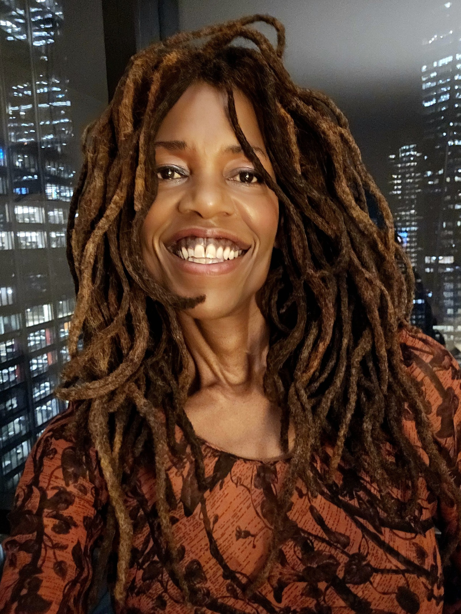 Lisa Teasley smiling in front of a window with city skyscrapers at night
