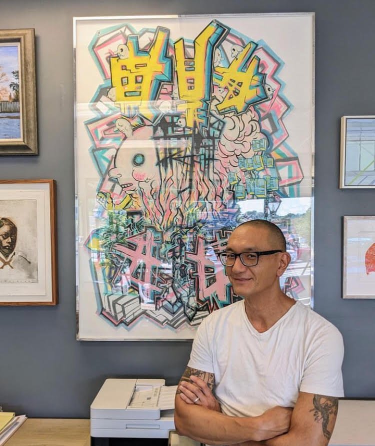 Oura Sananikone, arms crossed, in front of a large framed graffiti-style artwork