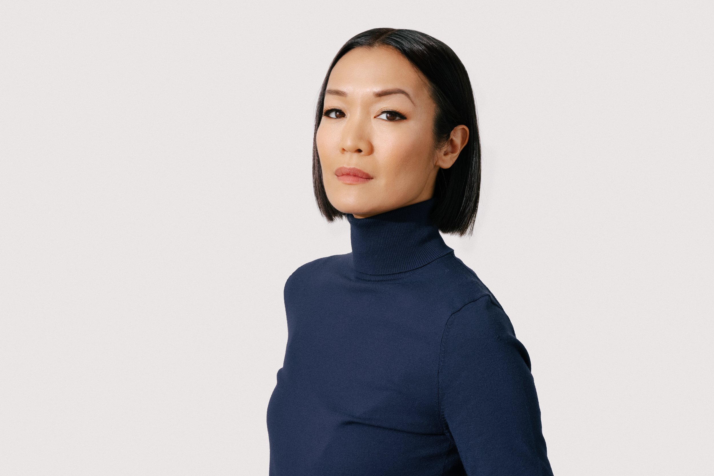 Sydney Viengluang in a navy turtleneck against a light gray backdrop