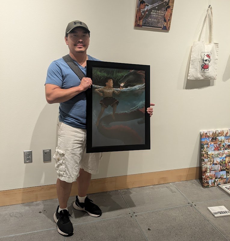 Tou Her holding his framed painting Temptation in a gallery