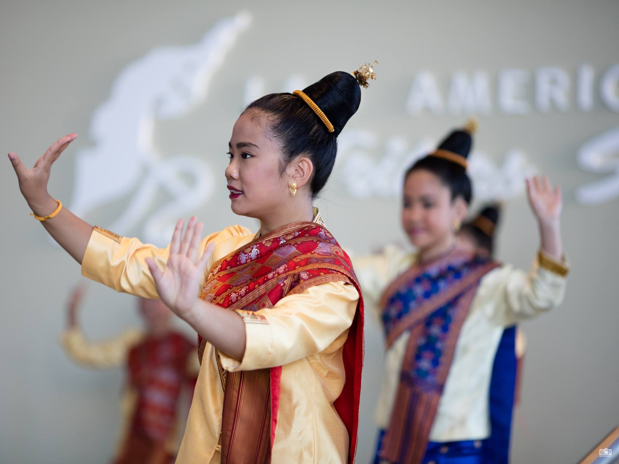 Young Lao dancers in gold blouses and silk pha biang sashes performing a traditional dance with graceful hand gestures