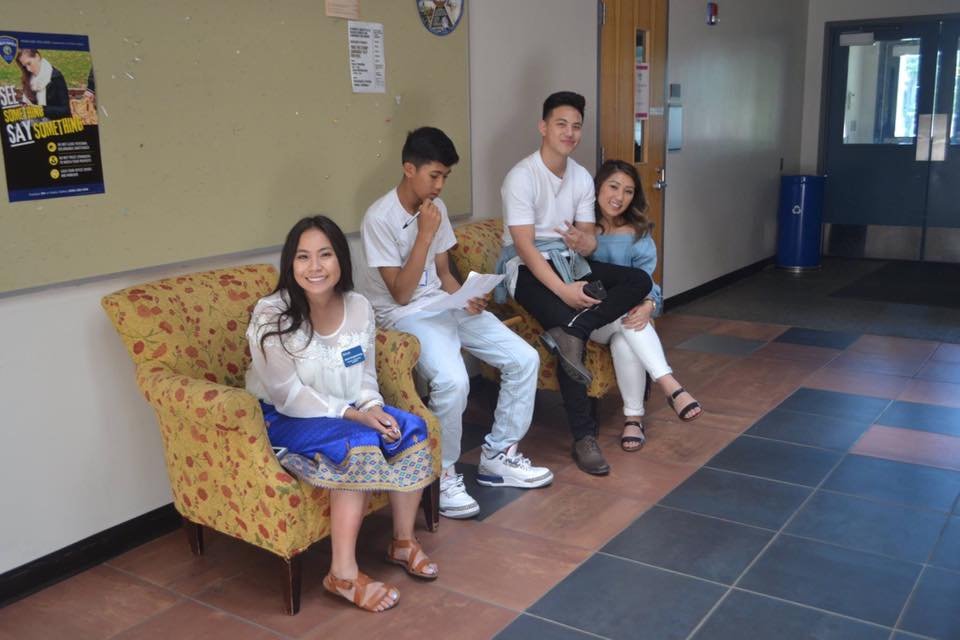 Four young people sitting on armchairs in a school hallway, one woman in a sinh smiling at the camera