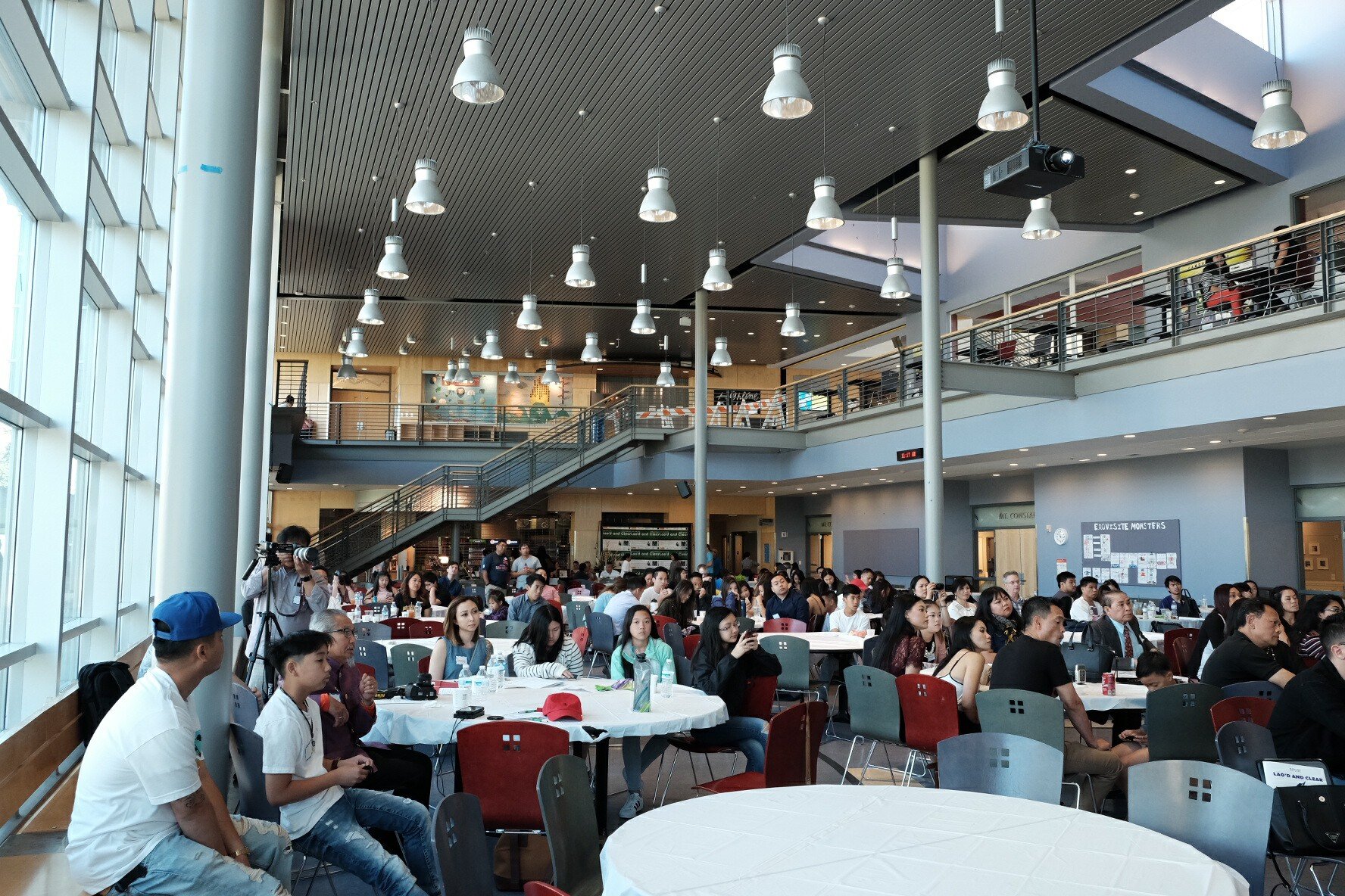 A large audience seated at round tables in a multi-level atrium at the Lao American Writers Summit