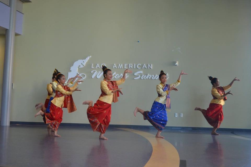 Young dancers in Lao costume with sinh skirts performing a traditional Lao dance in front of the Lao American Writers Summit sign